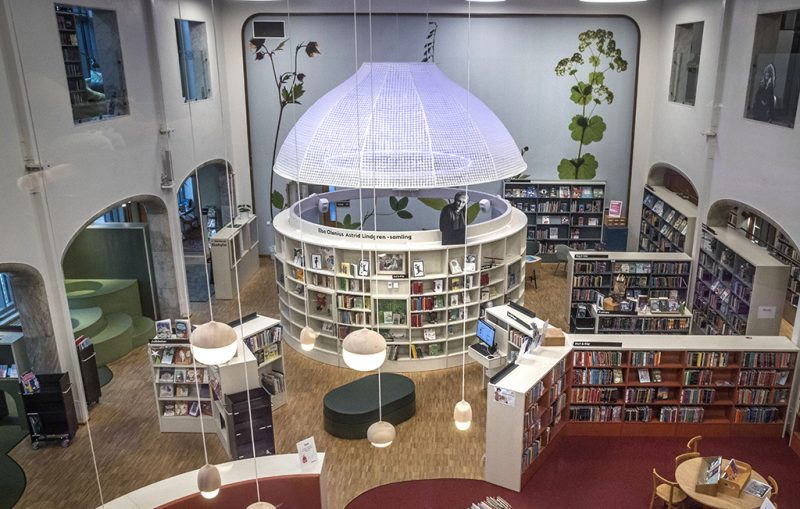 Vy över barnsavsdelningen i Tranströmerbiblioteket med bokhyllor och en stor lampa.